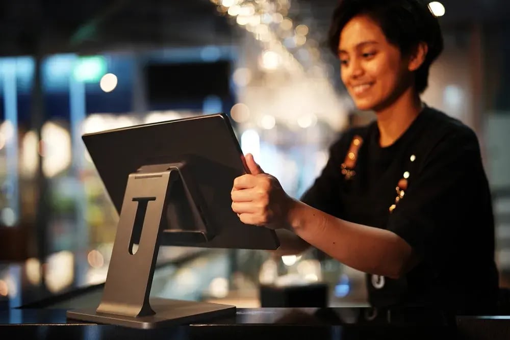 Cashier smiling while adjusting a Cliqbux point of sale screen at the counter