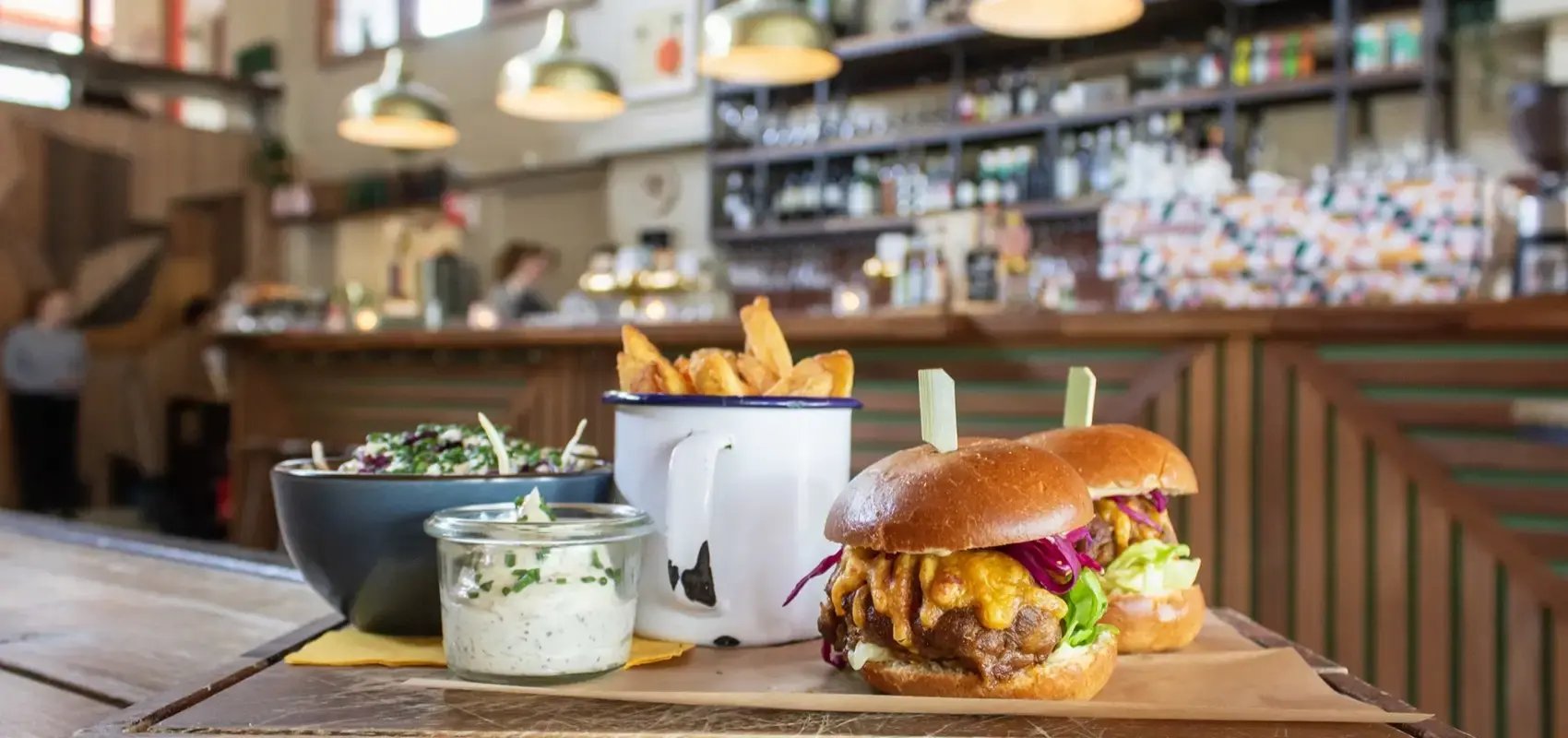 Two sliders, fries, and coleslaw served on a wooden counter in a busy restaurant